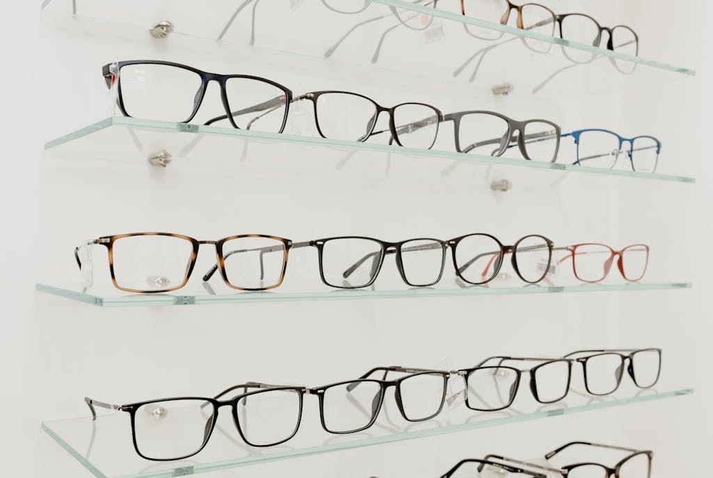 A variety of eyeglasses displayed on clear glass shelves in a retail store.